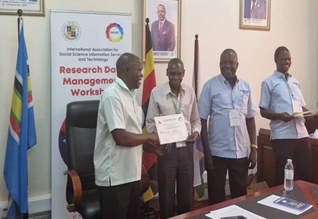 A black man in white T-shirt is handing over a certificate. A poster is behind them.